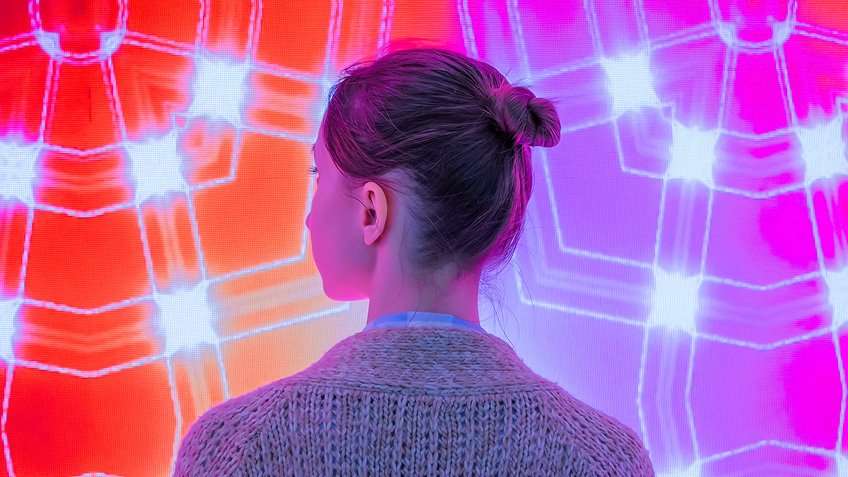 A woman facing away from the camera, facing a colourful wall