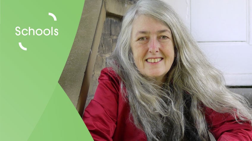 Photo of Mary Beard, a white woman with long grey hair wearing a red top. On the left is a green graphic overlay with white text that says 'Schools'.