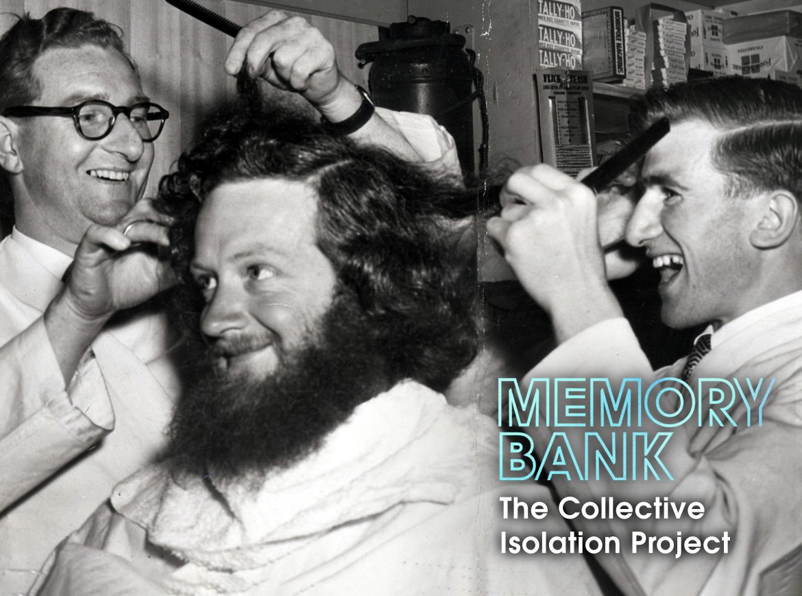 A man with a big beard and hair receives a trim while three other men look on smiling
