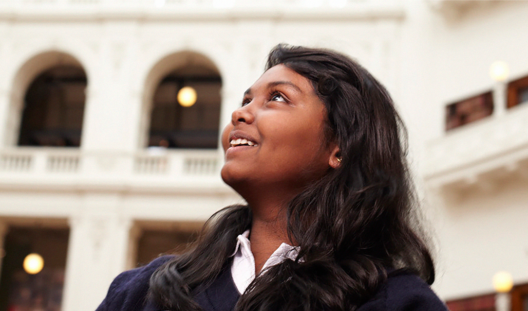 A woman with black hair looking up and smiling, with bright white walls behind her