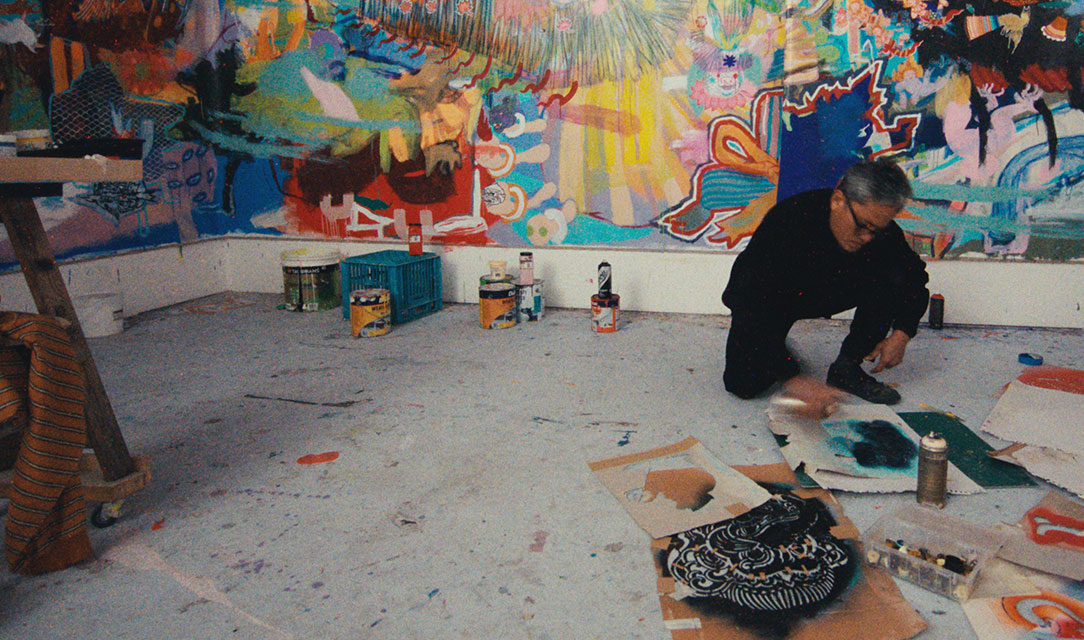 Image of artist Bundit Puangthong crouching on the ground and painting in his studio