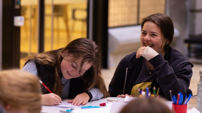 Two teenagers writing and laughing at a desk
