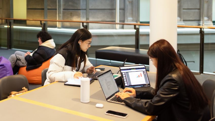 Two students with laptops and tablets sitting at a desk studying