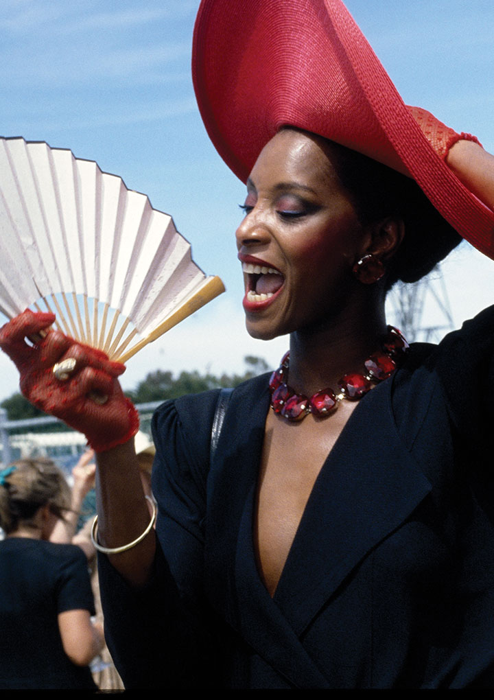 elegant looking lady wearing a black dress and red hat waving a fan