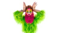 Person in neon green, shaggy shirt with a hot pink beard has hands behind head to make it look like they're a rabbit