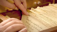 Fingers scroll through index cards in an old-fashioned library card catalogue