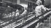 black and white photo of smiling woman on escalator reflected in mirrors