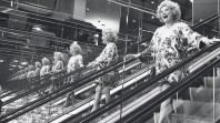 black and white photo of smiling woman on escalator reflected in mirrors
