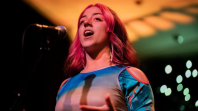 Photo of a woman with pink, shoulder-length hair speaking into a microphone