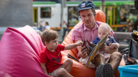 A close up of a parent reading a story to their two kids on the beanbags outside of the Library