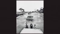 black and white photo of 3 smiling kids pushing a car through floodwaters