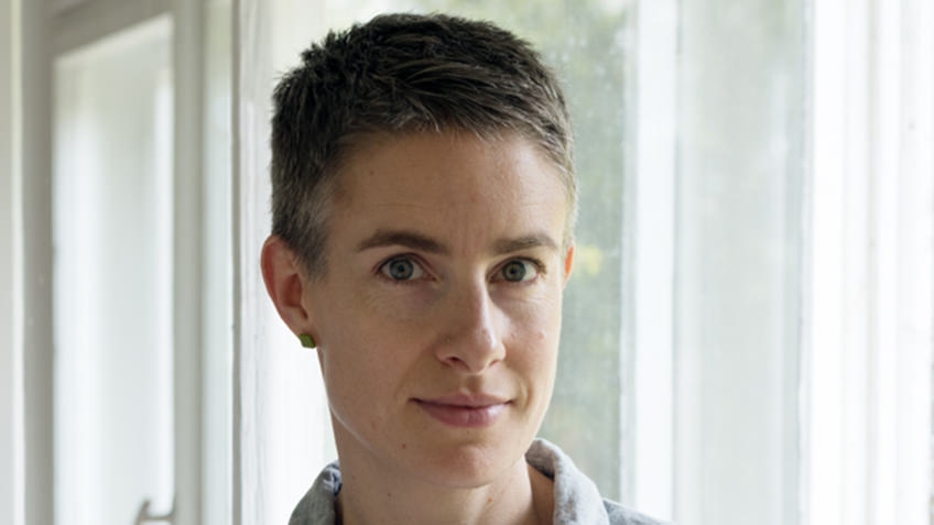 woman with short grey hair photographed backlit against white curtains