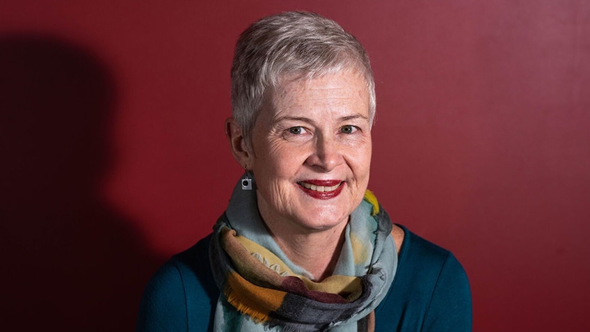 portrait of older woman wearing a scarf and teal jumper against red background