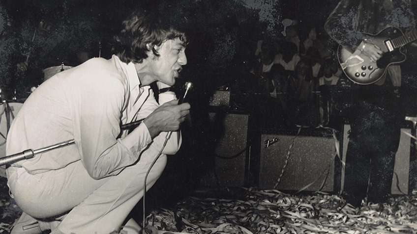 black and white 1960s photo of Mick Jagger crouching on the stage