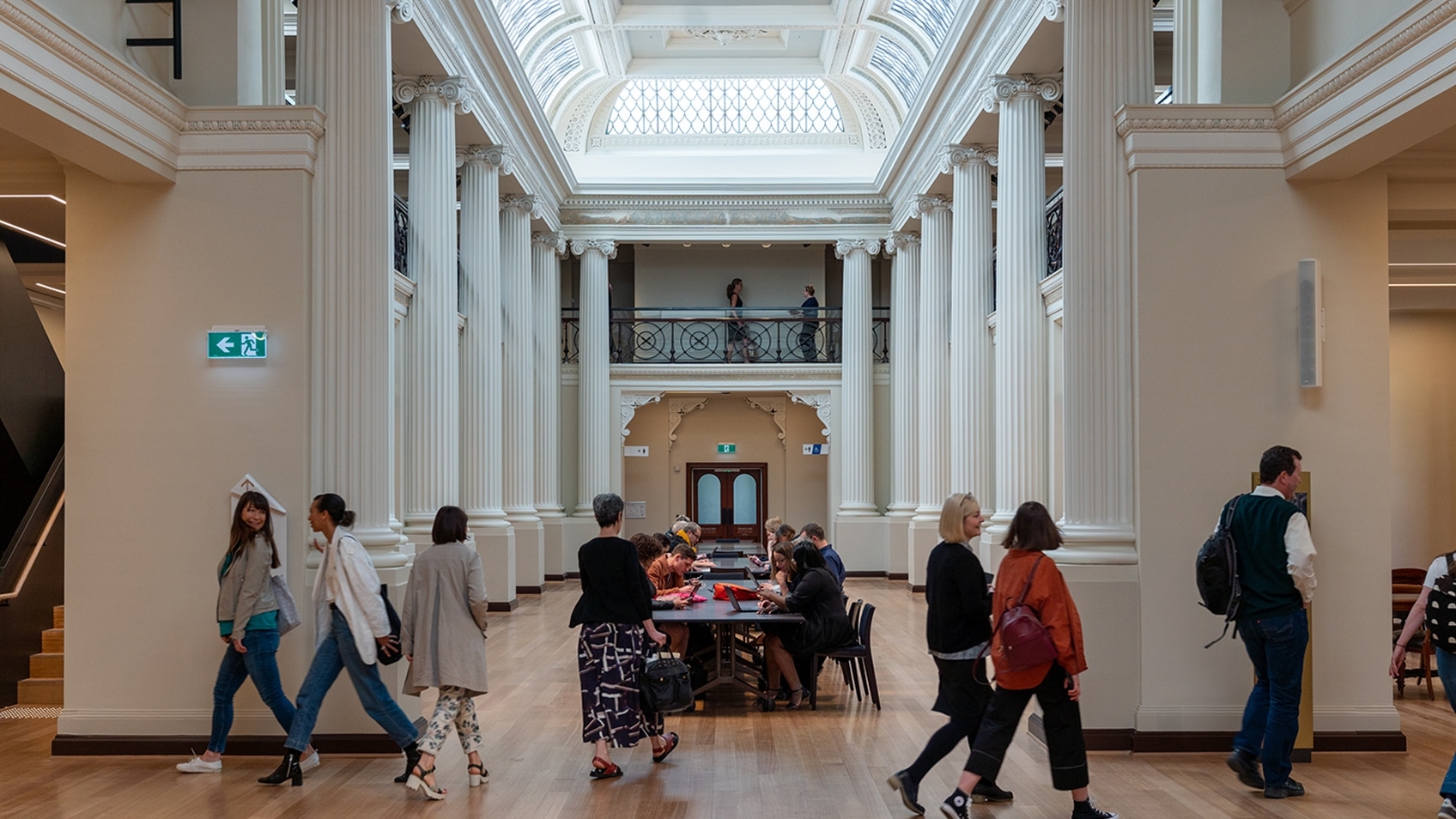 people walking past pillared hall with central tables