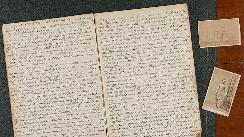 An old handwritten diary lays open beside photos of a US Confederate soldier and a clipper ship