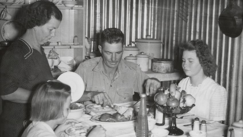 A black and white photograph of a family including a man, a woman and two children, gathered around a dinner table