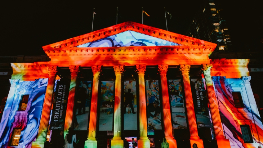 An exterior view of State Library Victoria at night, illuminated by colourful lights