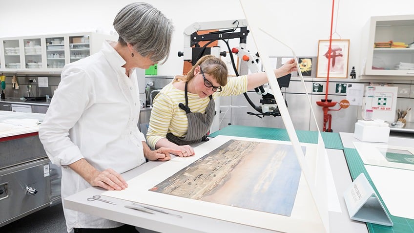 Colour photo of Liardet's watercolour being assessed by two staff in the State Library Conservation Lab