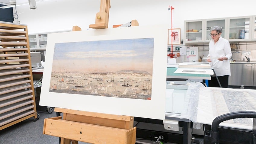Colour photo showing Liardet's watercolour on an easel in the State Library's Conservation Lab awaiting assessment