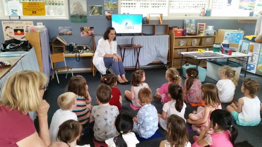 A woman on a chair reading to a large group of children