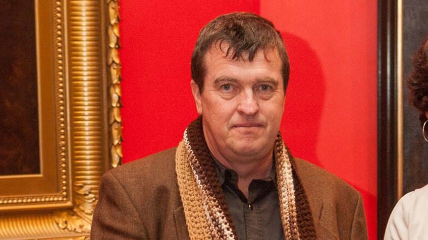 man wearing brown jacket against red background and oil paintings
