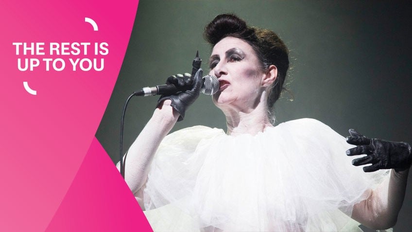 Brunette woman in white dress wearing black gloves holding a mic while performing