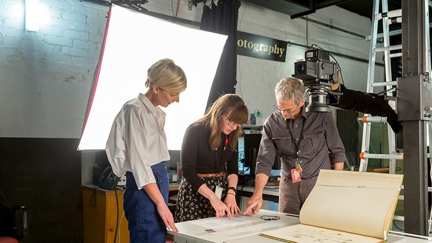 three people looking at a large book being photographed in a studio
