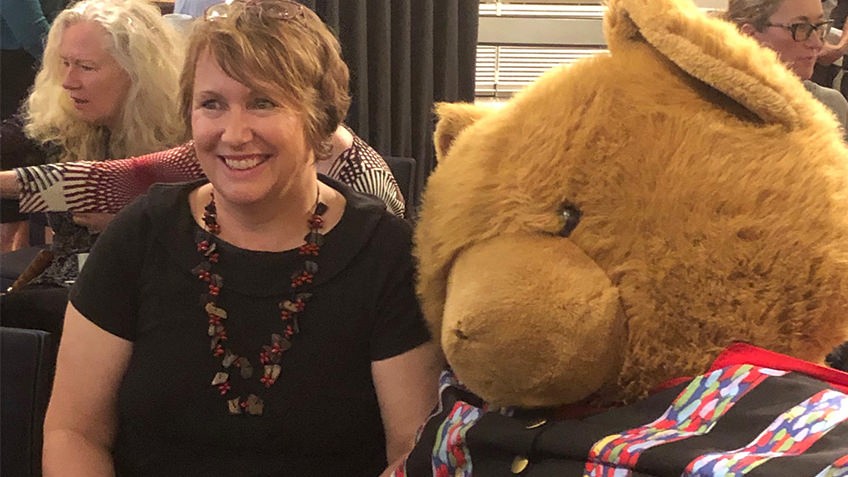 Smiling woman seated next to a giant teddy