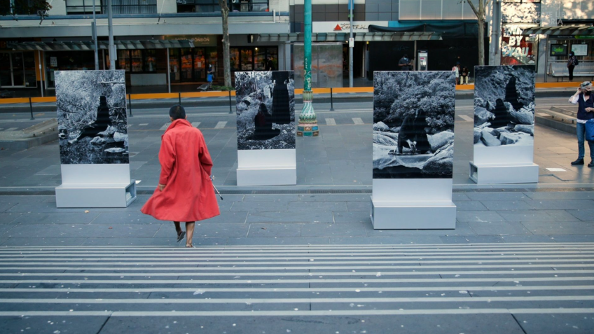 Woman in red coat standing in front of artworks outside State Library Victoria 