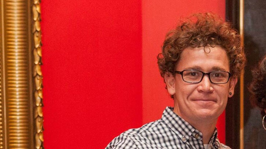 man with curly hair and glasses against a red background