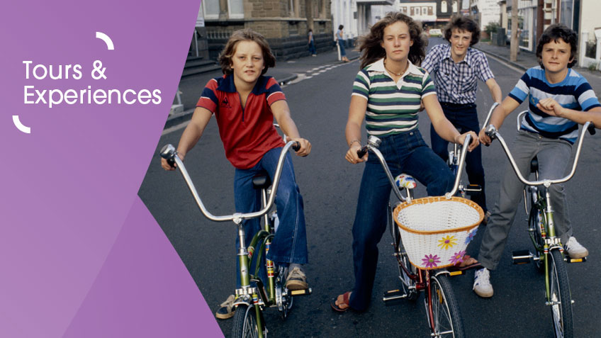 Group of four kids dressed in 70s attire on bikes facing camera