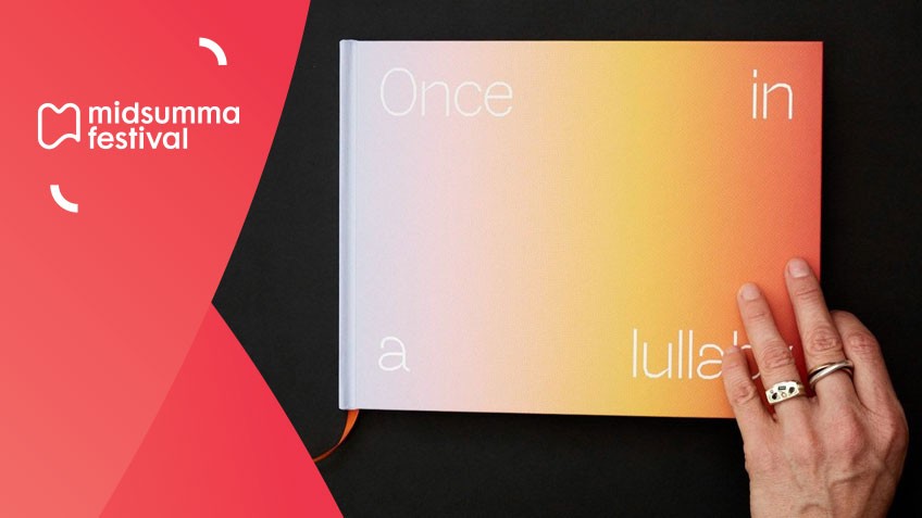 An image of a book with a rainbow gradient and the words 'Once Upon a Lullaby' on this. Hand holding book.