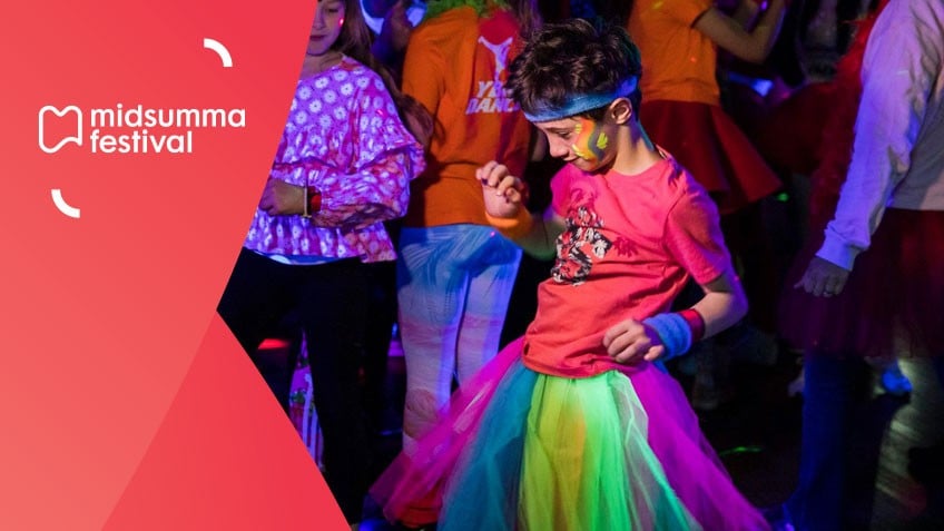 Boy wearing bandanna, pink shirt and ranbow tulle skirt is mid-dance