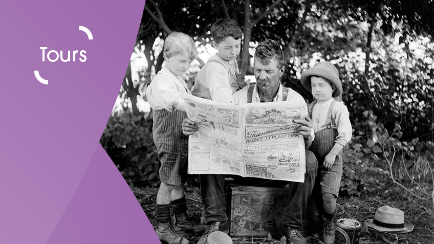 A black and white image of kids huddled around a father looking at the local newspaper.