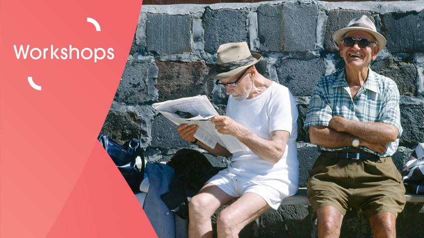 Two older gentleman sitting down wearing summer clothing, one of them is reading a newspaper