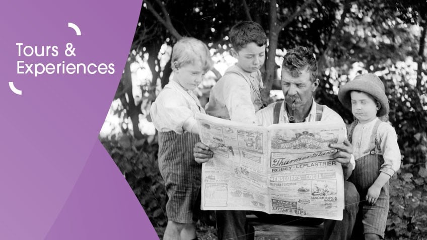 Black and white photograph of an adult man reading a newspaper with three children next to him. They are outside, and there are bushes and trees behind them. On the left is a purple graphic overlay with white text that says tours and experiences.