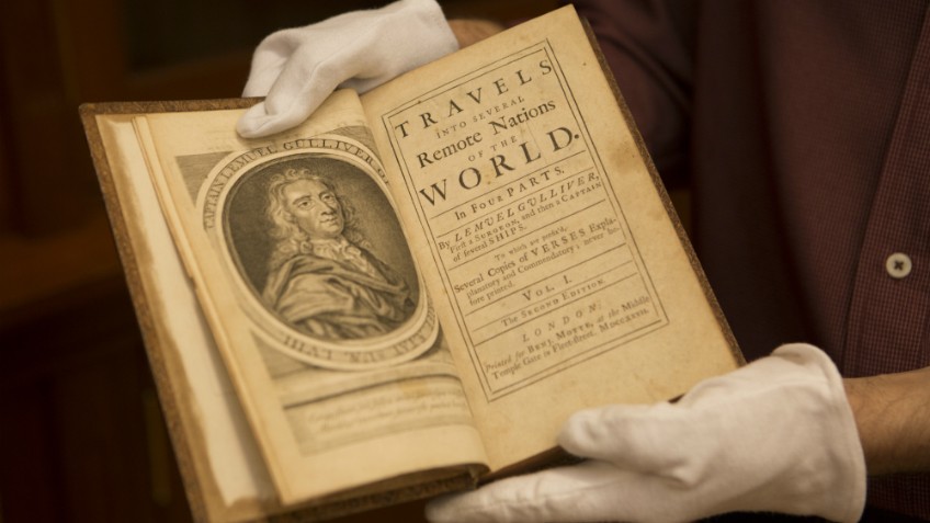Colour photo of gloved hands holding a rare early edition of Jonathan Swift, Travels into several remote regions of the world…by Lemuel Gulliver, London, 1727