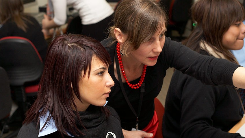 A teacher assists a female Year 12 student at a computer