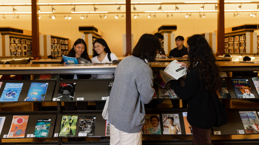 Image of library visitors and patrons looking at books and magazines on shelves in the Redmond Barry Reading Room.