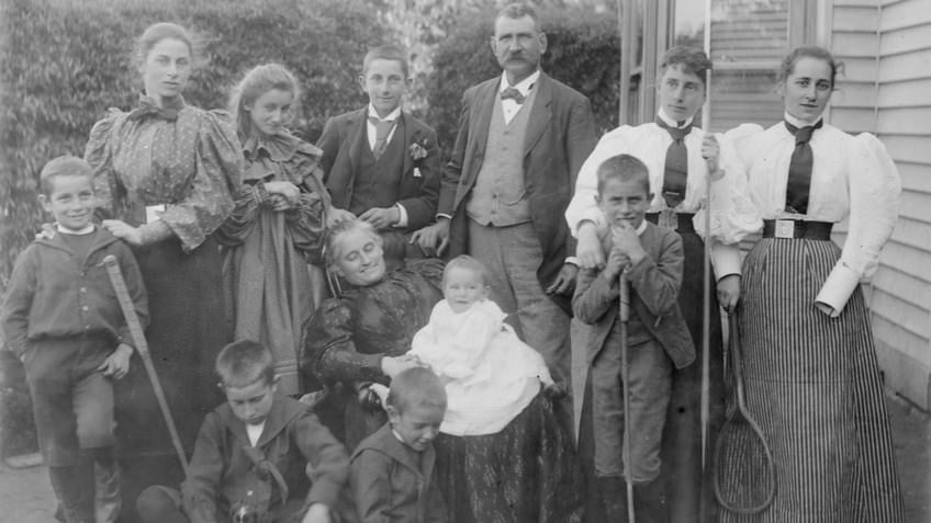 Group of women, children, grandmother nursing baby and a man, all whole-length, standing and sitting
