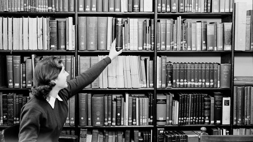 Librarian reaching for books on library shelf