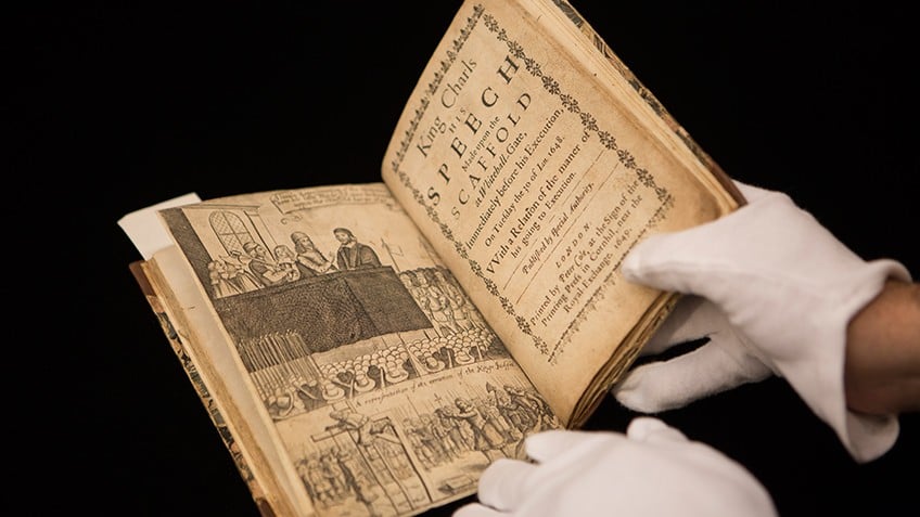 Photo of a book containing a notice about King Charles' execution being held by a person wearing white gloves