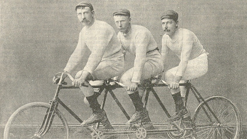 Sepia image of three Victorian-era men riding a tandem bicycle