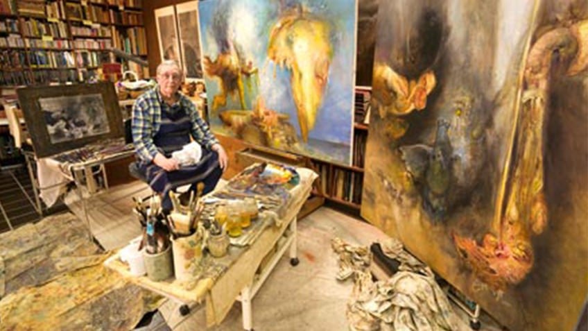 Colour photo of Australian surrealist painter James Gleeson at work in his studio with canvases and dropsheets