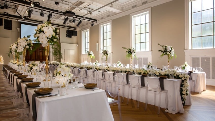 Three rows of long tables covered in white tablecloths and strewn with flowers
