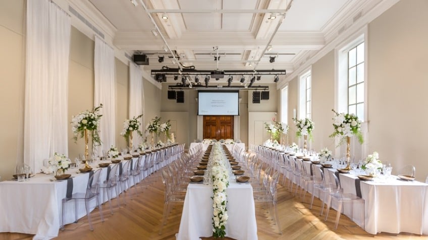 Three rows of long tables covered in white tablecloths and strewn with flowers