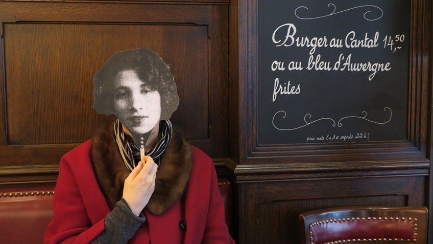 french cafe with blackboard menu and woman in red coat holding up the black and white facemask of a woman