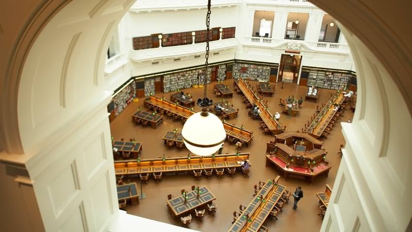 Colour aerial view of State Library Victoria's La Trobe Reading Room interior, taken from a top-floor balcony under the dome, showing desks