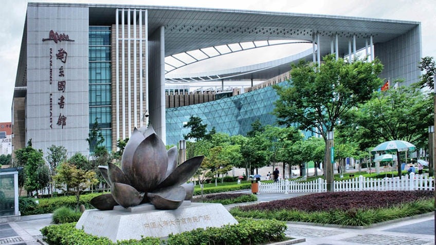 Modern Chinese building with lotus sculpture, curved glass walls, trees and gardens